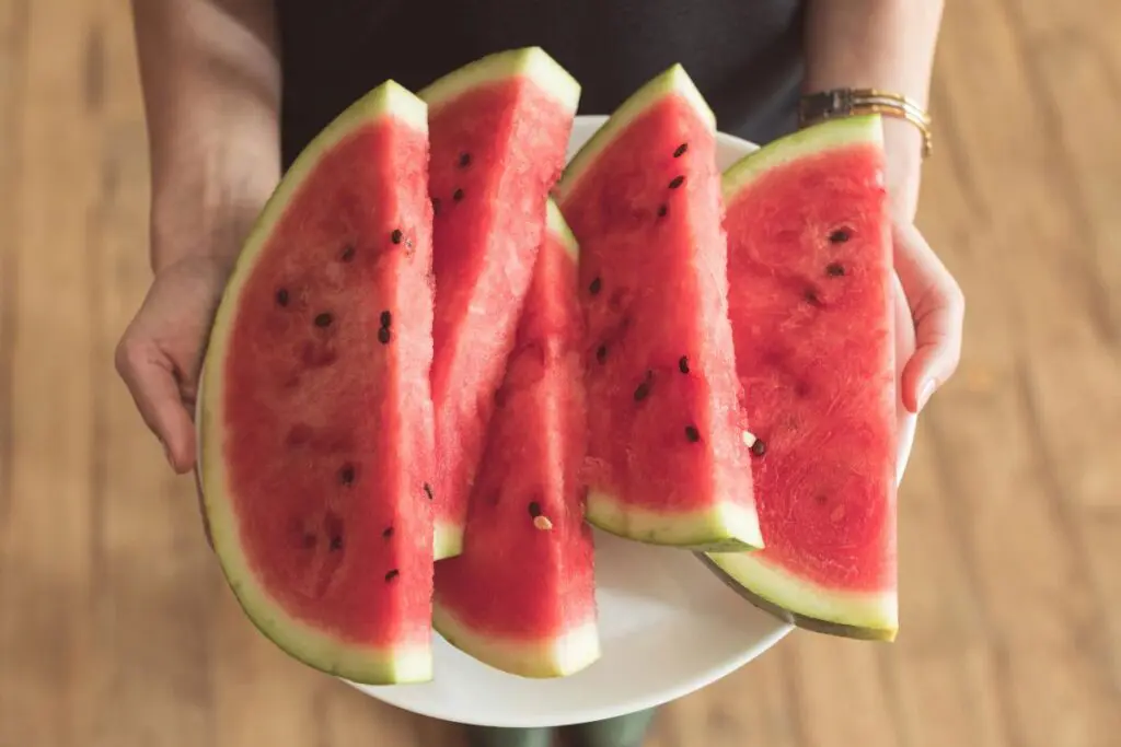 A person holding a plate with several slices of watermelon.