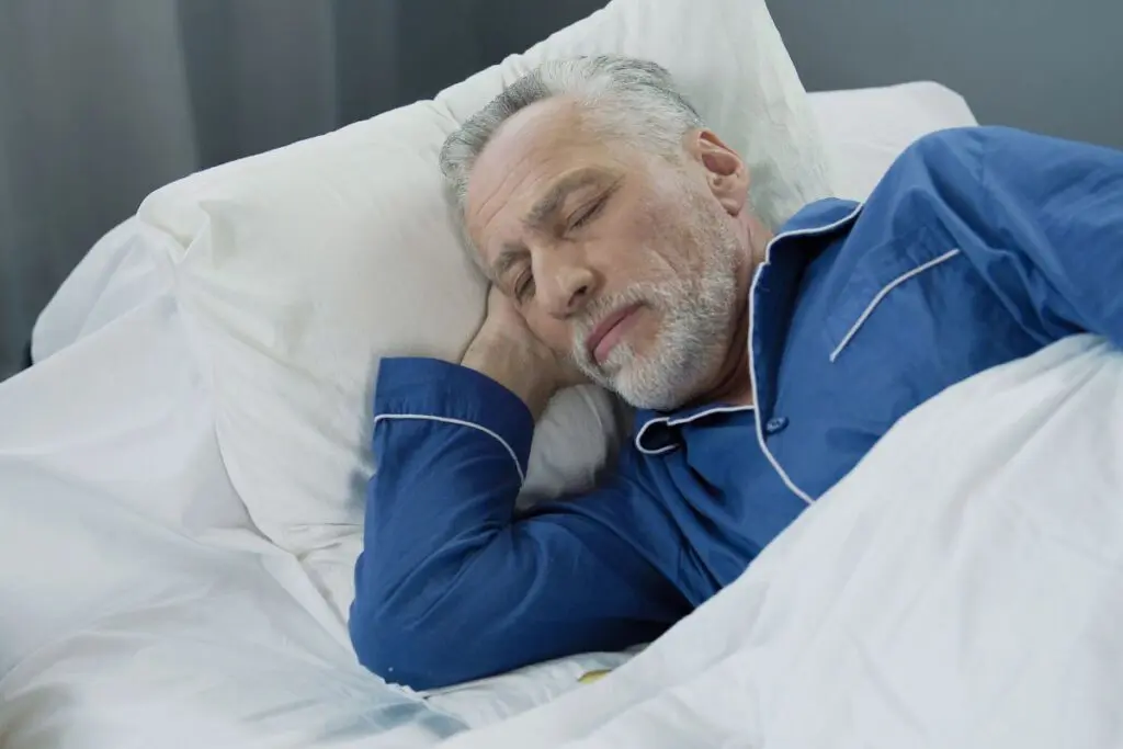 A senior man with gray hair, wearing blue pajamas, sleeping peacefully in a bed.