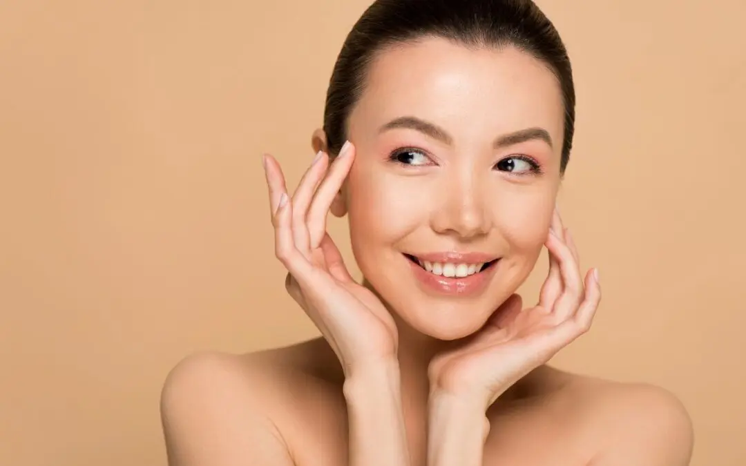 A woman with a joyful expression, posing with her hands on her cheeks against a neutral background.