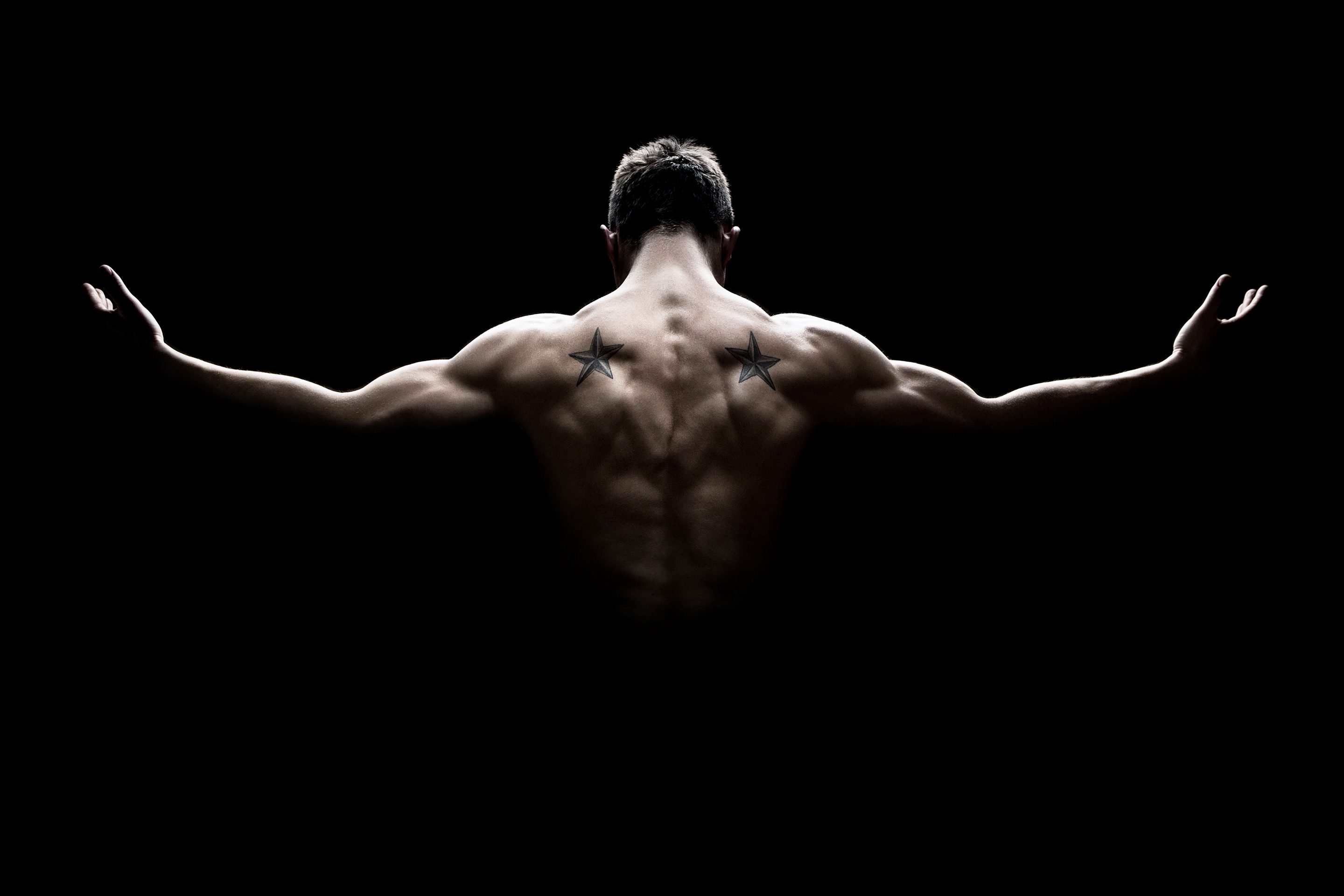 A man flexing his back muscles on a black background