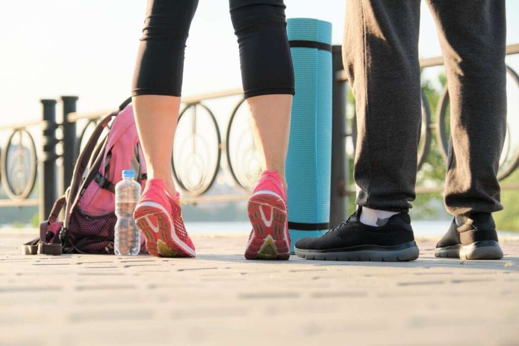 Two people exercising, next to a bottled water, backpack and a yoga mat.