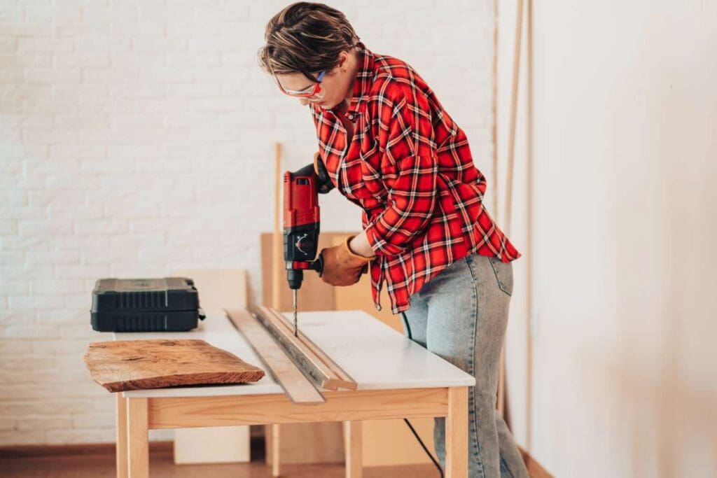 A girl drilling plank with drill on the table.