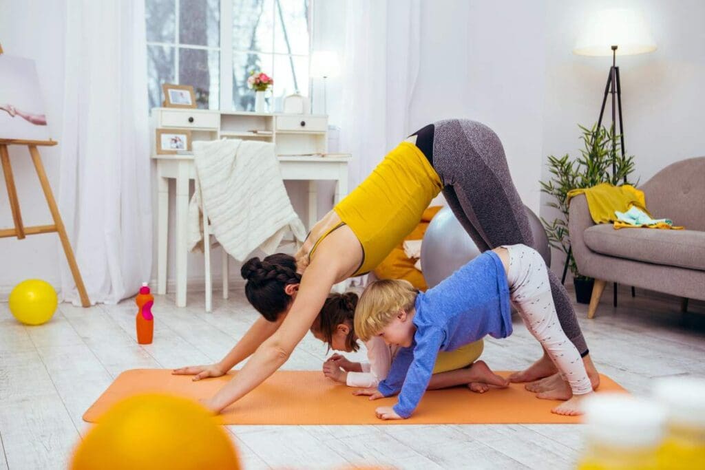 A woman and two children practice yoga together on an orange mat in a bright living room.
